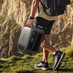 Person trägt die Anker Solix C1000 Gen 2 Portable Power Station beim Wandern über eine Felslandschaft; kompakte Abmessungen am Gerät sichtbar.